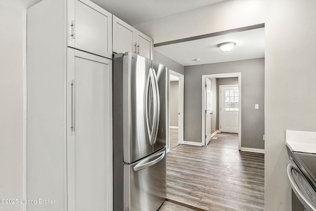 kitchen featuring light countertops, appliances with stainless steel finishes, white cabinetry, wood finished floors, and baseboards