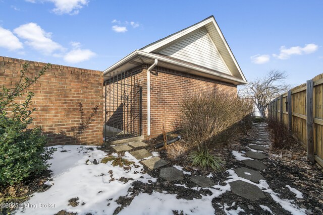 view of snowy exterior with brick siding and fence