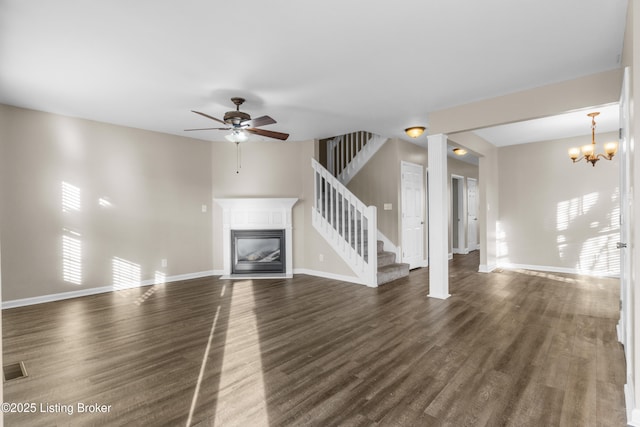 unfurnished living room featuring dark wood-type flooring, a glass covered fireplace, baseboards, and stairs