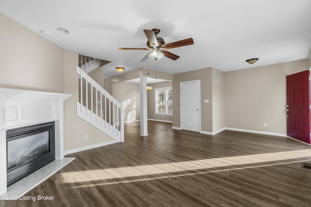 unfurnished living room featuring stairs, a glass covered fireplace, dark wood finished floors, and baseboards