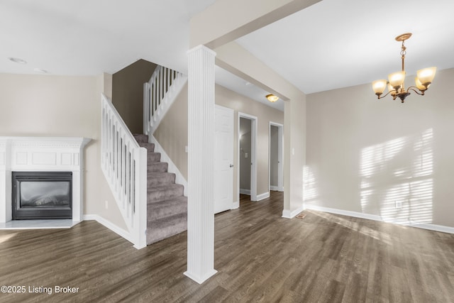 unfurnished living room with a notable chandelier, dark wood-type flooring, a glass covered fireplace, and baseboards