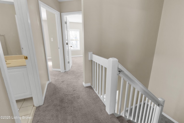 hallway with baseboards, an upstairs landing, and light colored carpet