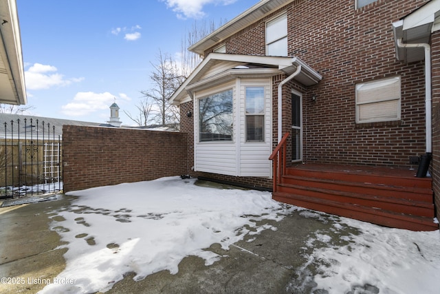 snow covered property featuring entry steps, brick siding, and fence