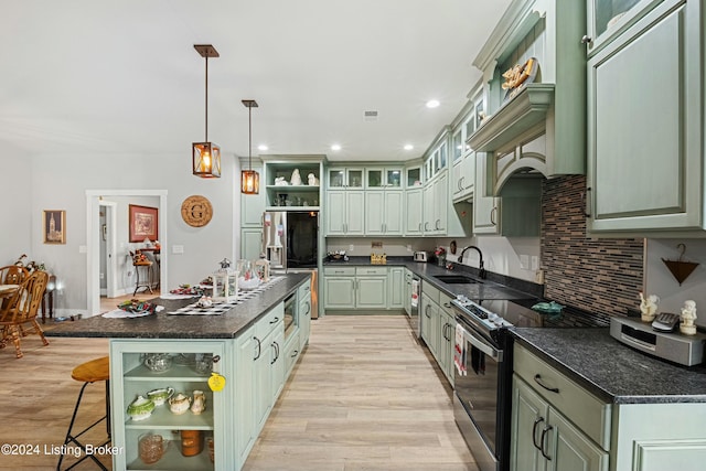 kitchen with stainless steel appliances, green cabinets, open shelves, an island with sink, and dark countertops