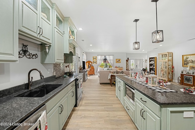 kitchen with stainless steel appliances, light wood-style flooring, glass insert cabinets, open floor plan, and a sink