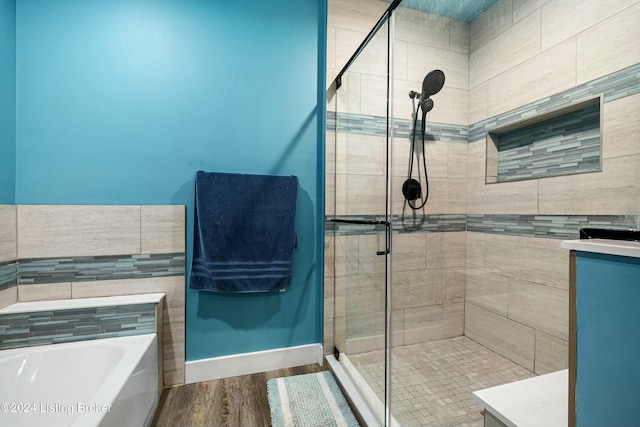 full bath with baseboards, wood finished floors, a garden tub, vanity, and a shower stall