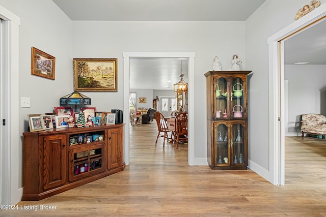 hall featuring light wood-type flooring, baseboards, and an inviting chandelier