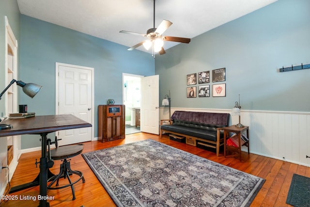 living area with a ceiling fan, wainscoting, and wood finished floors