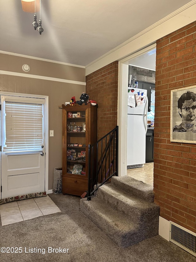 entrance foyer featuring ornamental molding, brick wall, and light carpet