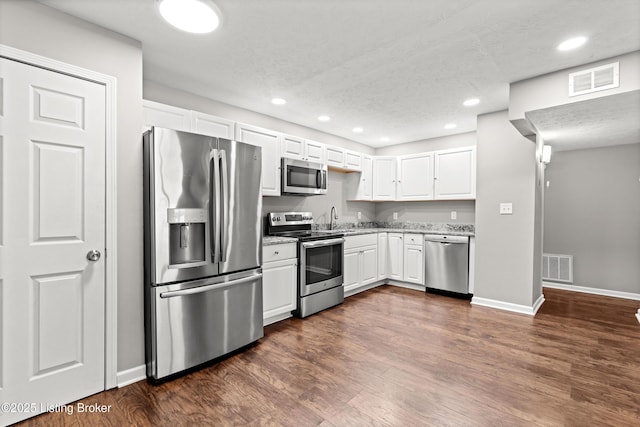 kitchen featuring appliances with stainless steel finishes, white cabinetry, dark hardwood / wood-style flooring, and light stone countertops