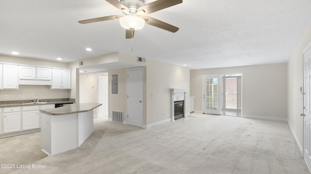 kitchen with white cabinetry, light colored carpet, a kitchen island, electric panel, and sink