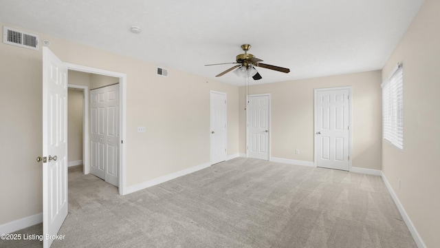 unfurnished bedroom with light carpet, ceiling fan, and multiple closets