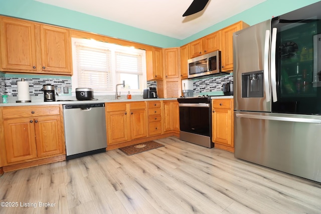 kitchen with light wood-type flooring, sink, backsplash, ceiling fan, and appliances with stainless steel finishes