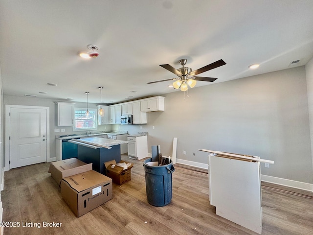 kitchen featuring a kitchen island, stainless steel microwave, hanging light fixtures, light countertops, and white cabinetry