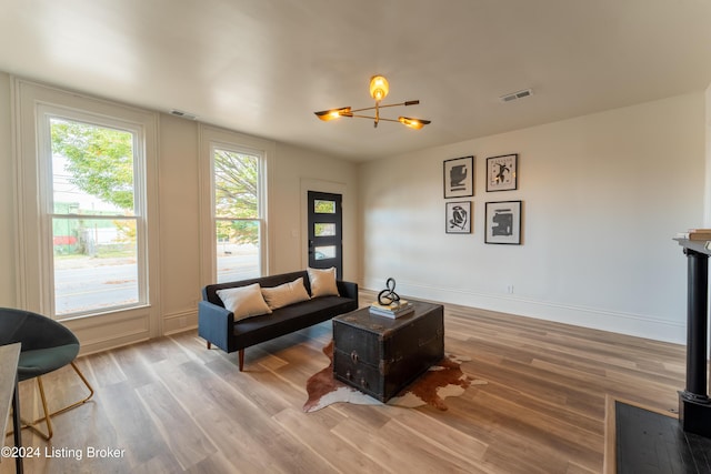 living room featuring a notable chandelier, wood finished floors, visible vents, baseboards, and a wood stove