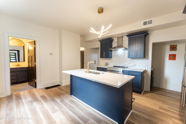 kitchen with a sink, visible vents, light countertops, wall chimney range hood, and a center island with sink