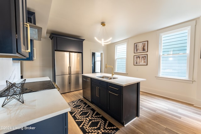 kitchen with pendant lighting, stainless steel appliances, light countertops, a sink, and an island with sink