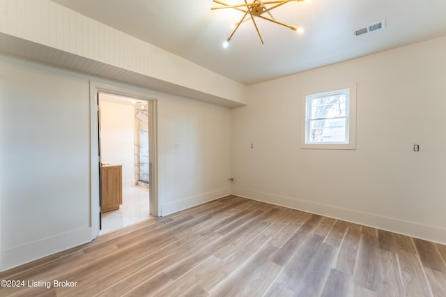 empty room with an inviting chandelier, light wood-style flooring, visible vents, and baseboards