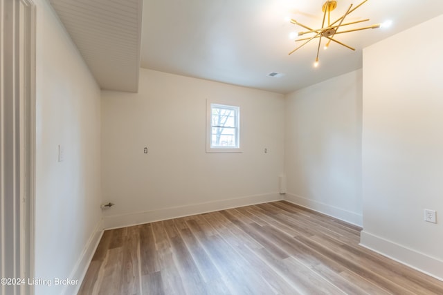 empty room with an inviting chandelier, light wood-type flooring, visible vents, and baseboards