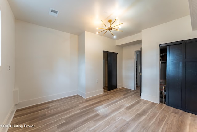 unfurnished bedroom featuring visible vents, a notable chandelier, light wood-style flooring, and baseboards