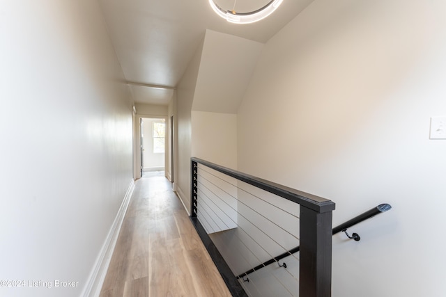 corridor featuring light wood-type flooring, an upstairs landing, and baseboards