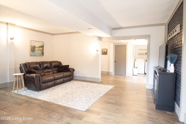 living room featuring washing machine and dryer, visible vents, baseboards, and wood finished floors