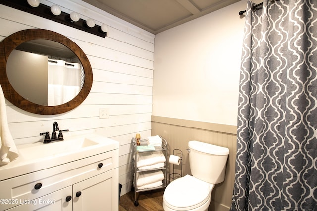 bathroom with toilet, a wainscoted wall, wood finished floors, vanity, and wood walls