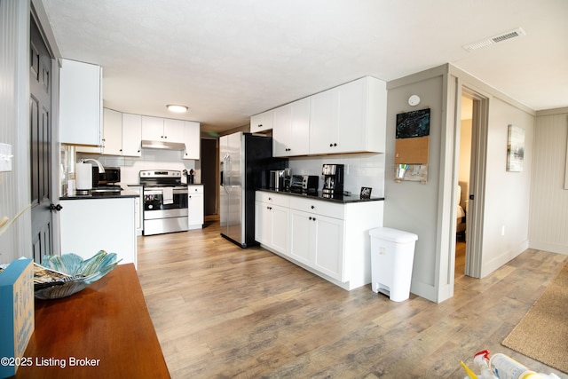 kitchen featuring light wood finished floors, dark countertops, stainless steel appliances, white cabinetry, and a sink