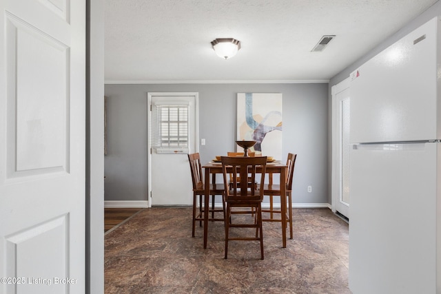 dining room with crown molding, visible vents, stone finish floor, a textured ceiling, and baseboards