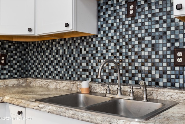 kitchen with light countertops, backsplash, a sink, and white cabinetry