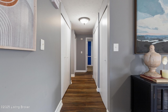 hall featuring a textured ceiling, dark wood-style flooring, and baseboards