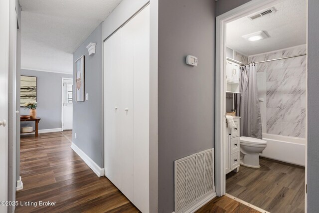 corridor with a textured ceiling, dark wood-style flooring, visible vents, and baseboards