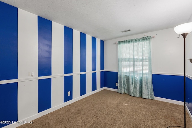 carpeted empty room with wallpapered walls, baseboards, visible vents, and a textured ceiling