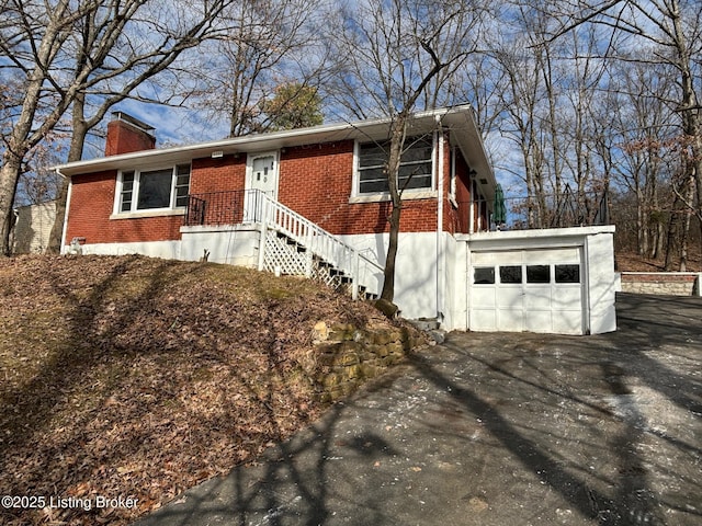 view of front facade with a garage, brick siding, driveway, and a chimney