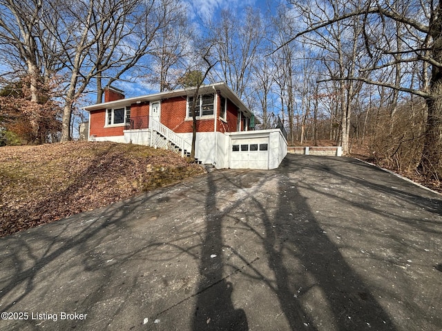 view of side of property featuring aphalt driveway, brick siding, a chimney, and a garage