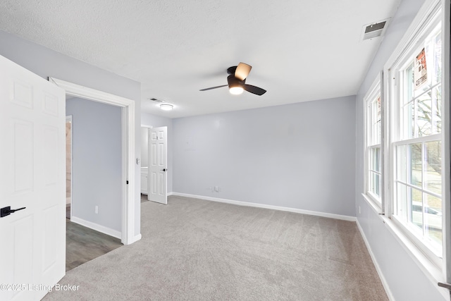 empty room featuring plenty of natural light, dark carpet, visible vents, and baseboards