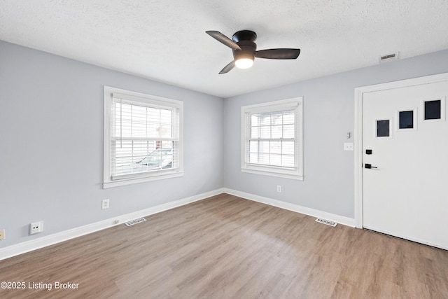 foyer entrance with baseboards, visible vents, light wood-style flooring, and a textured ceiling