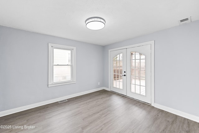 unfurnished room with a wealth of natural light, french doors, visible vents, and dark wood finished floors