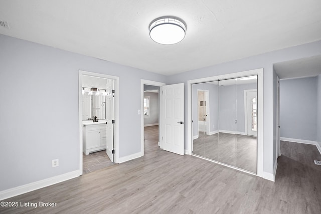 unfurnished bedroom featuring light wood-type flooring, ensuite bath, baseboards, and a closet