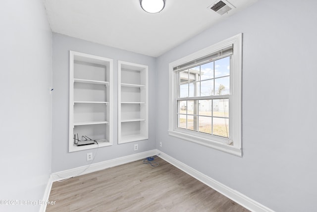 empty room with light wood-style floors, built in features, visible vents, and baseboards