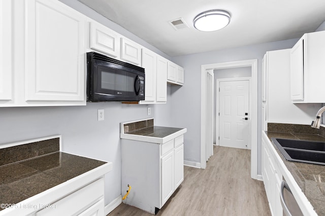 kitchen featuring tile counters, visible vents, white cabinets, a sink, and black microwave