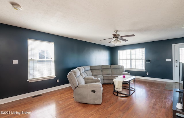 living area with visible vents, a textured ceiling, baseboards, and wood finished floors