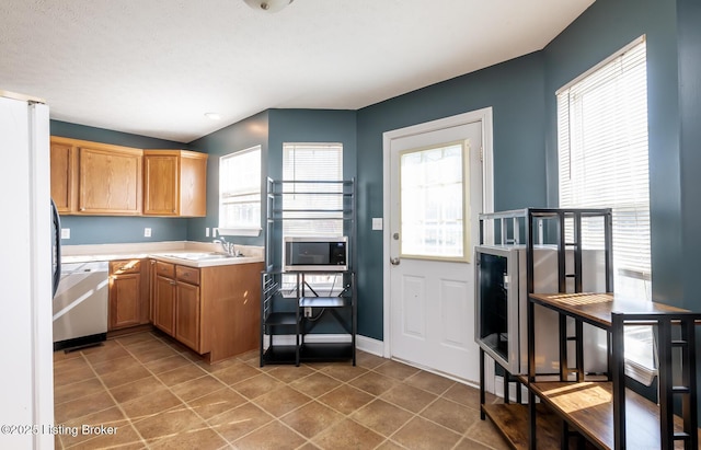 kitchen with dishwashing machine, stainless steel microwave, freestanding refrigerator, light countertops, and a sink