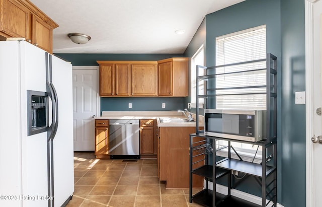 kitchen featuring stainless steel appliances, brown cabinetry, light countertops, and a sink