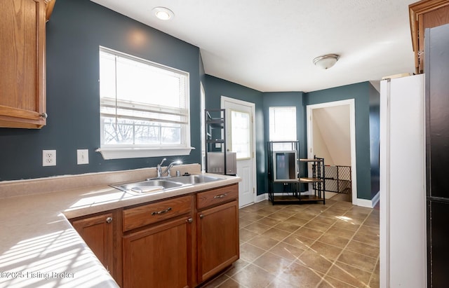 kitchen with light countertops, brown cabinetry, a sink, and a wealth of natural light