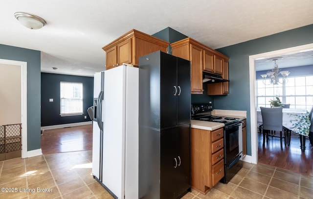 kitchen with a healthy amount of sunlight, under cabinet range hood, black / electric stove, and brown cabinets