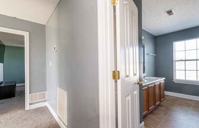 hallway with visible vents, a textured ceiling, and baseboards