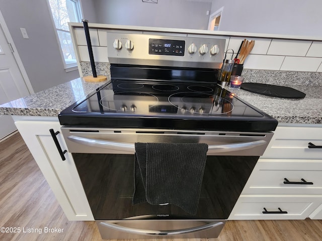 kitchen featuring light stone counters, light wood-style flooring, white cabinets, and stainless steel electric stove