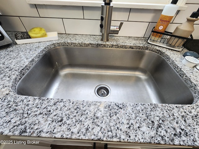 interior details with stone counters, a sink, and decorative backsplash