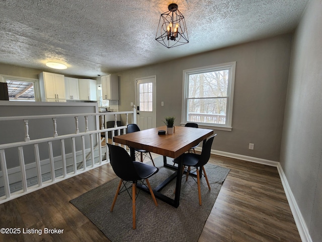 dining room featuring a notable chandelier, dark wood finished floors, a textured ceiling, and baseboards